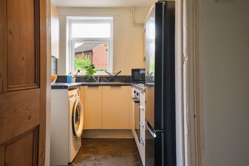 Small kitchen with yellow cabinetry, washing machine, window overlooking garden