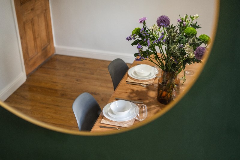 Dining table with place settings, chairs, and purple flowers in vase