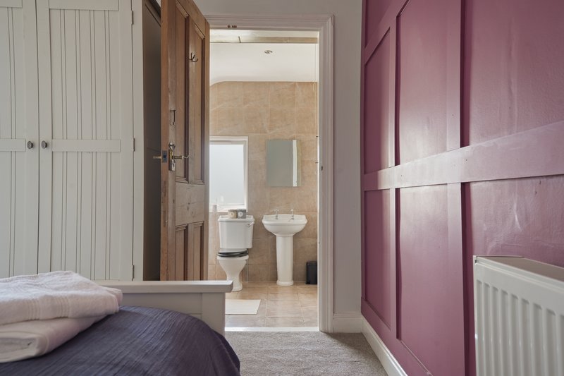 Bedroom with double bed, purple feature wall, and ensuite bathroom visible through open door