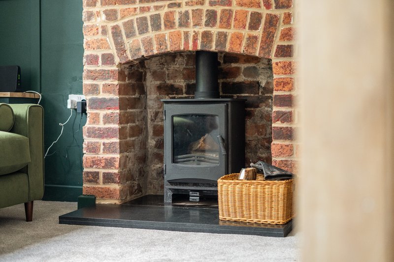 Brick fireplace with black wood-burning stove, wicker basket, and green armchair