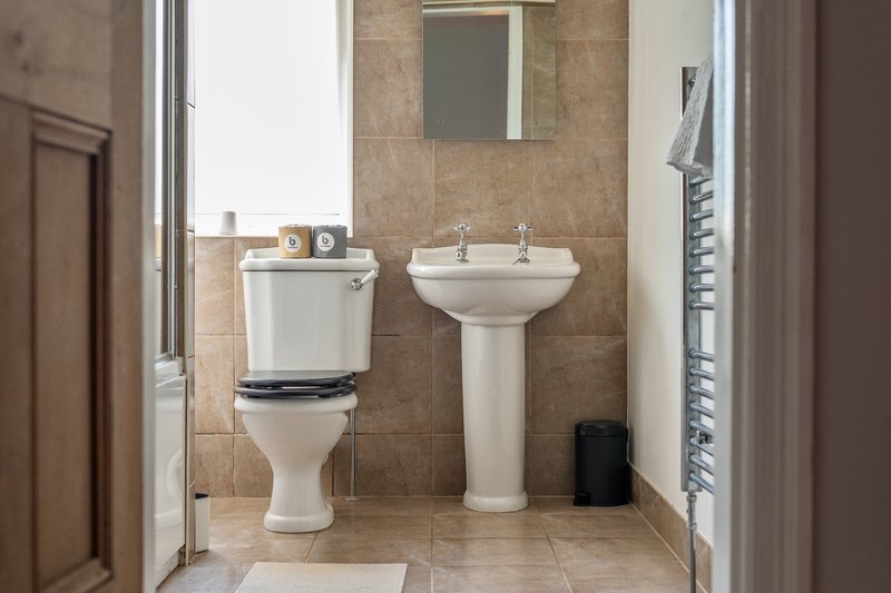 Bathroom with toilet, pedestal sink, mirror, towel rail and beige tile walls