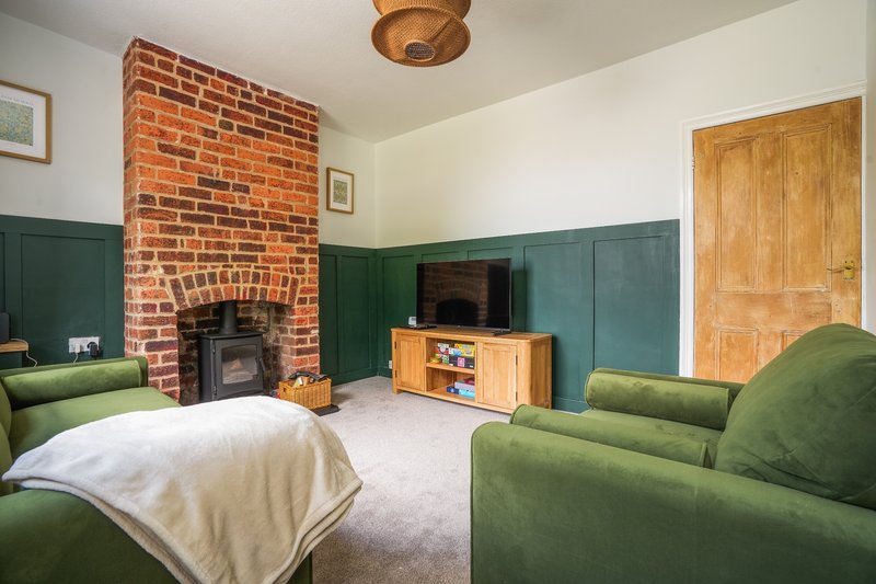 Spacious bedroom with fireplace, green panelling, exposed brick chimney, and armchairs