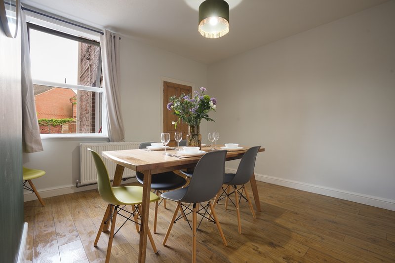 Modern dining room with wooden table, colorful chairs, and window overlooking brick building