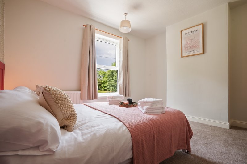 Bedroom with double bed, pink bedding, window with curtains, framed artwork