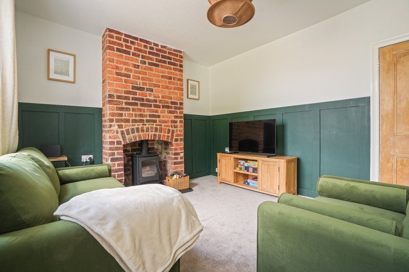 Living room with green panelled walls, brick fireplace, wood furniture and green upholstered seating