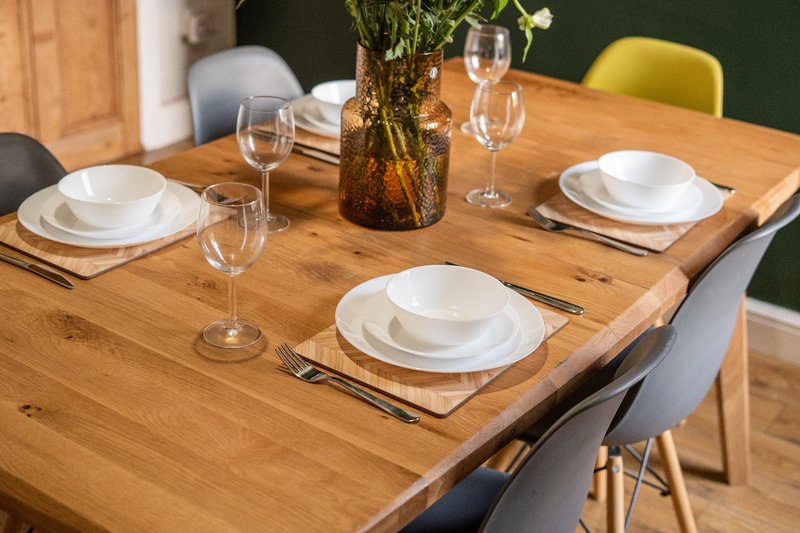Wooden dining table set for three with white plates, glasses, cutlery and flower centerpiece