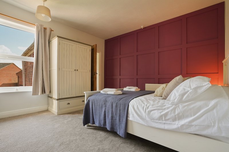 Bedroom with double bed, burgundy accent wall, wardrobe, and window overlooking brick building