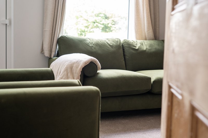 Bright living room with green upholstered sofa, cream throw blanket, and window with garden view