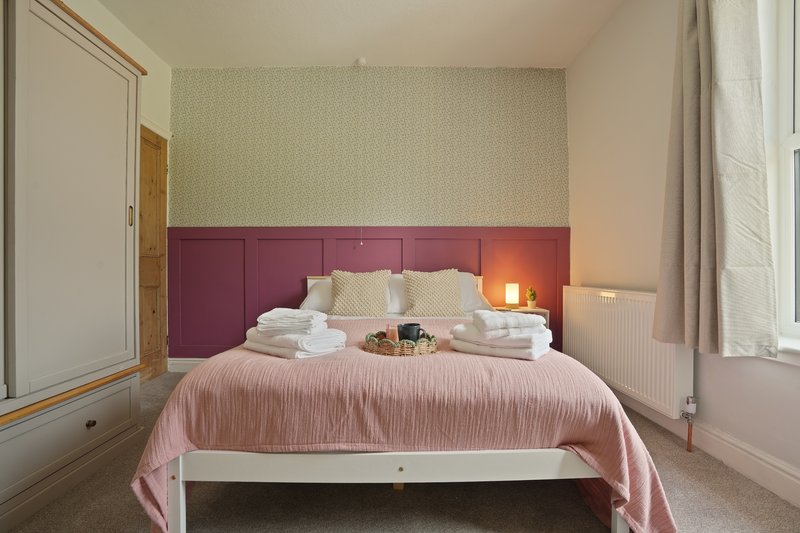 Bedroom with double bed, pink bedspread, burgundy headboard and neutral walls
