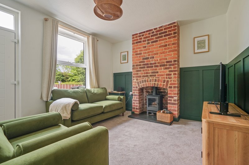 Spacious living room with green sofas, brick fireplace, wood TV unit and large windows