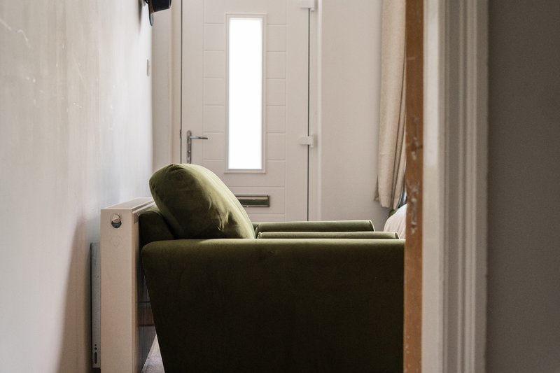 Hallway with olive green armchair, white door with glazed panel, and cream curtains