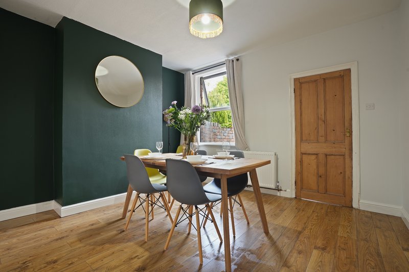 Dining room with wooden table, black chairs, dark green accent wall and round mirror