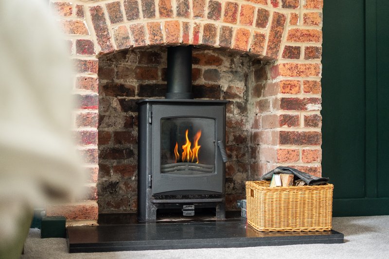 Black wood-burning stove in brick fireplace with wicker basket beside it