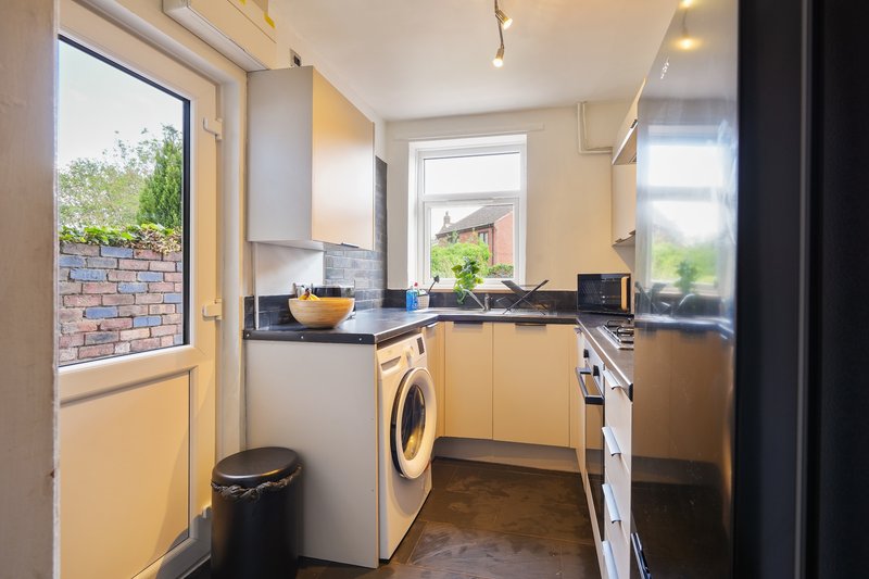 Compact kitchen with yellow cabinetry, washing machine, black countertop and garden view