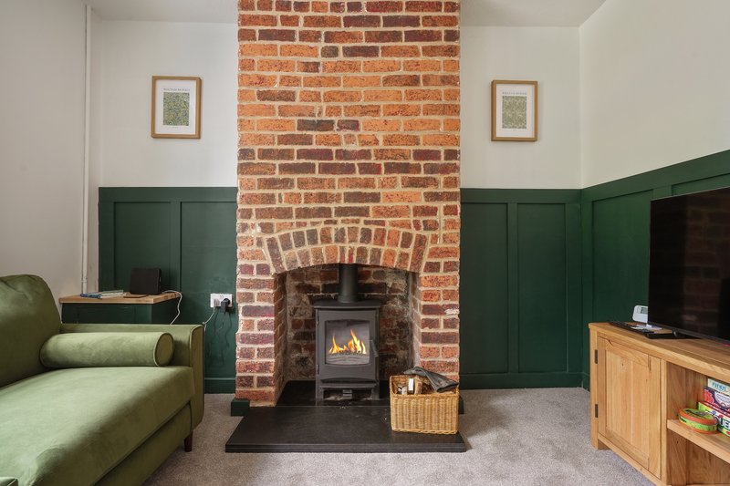 Living room with green sofa, brick fireplace with wood stove, and wooden TV unit