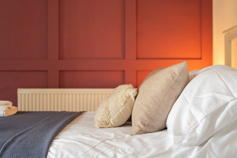 Bedroom with white bedding, beige cushions, dark throw, and red panelled wall
