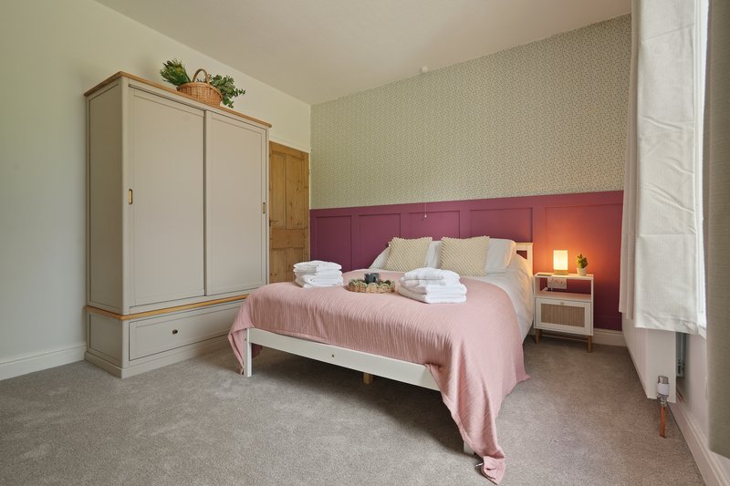 Bedroom with double bed, pink bedding, burgundy headboard, wardrobe and bedside lamp