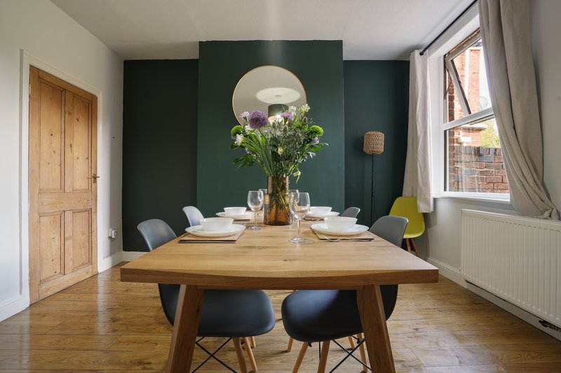 Dining room with wooden table, black chairs, floral centerpiece and dark green accent wall
