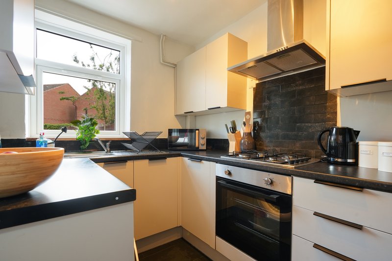 Modern kitchen with white and wood cabinetry, black countertops, gas stove and window view