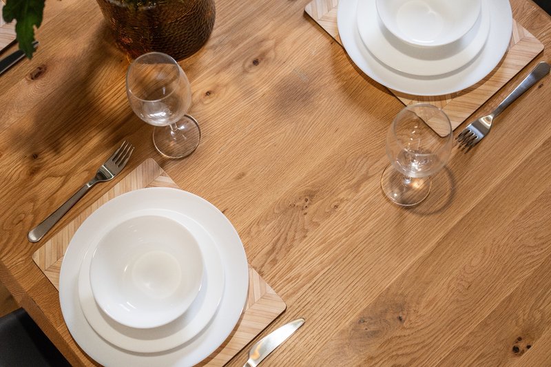 Wooden dining table set with white plates, glasses, cutlery and napkins