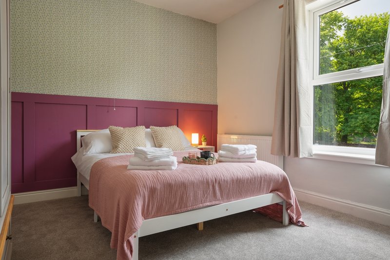 Modern bedroom with pink upholstered headboard, double bed, bedside lamps and large window overlooking garden