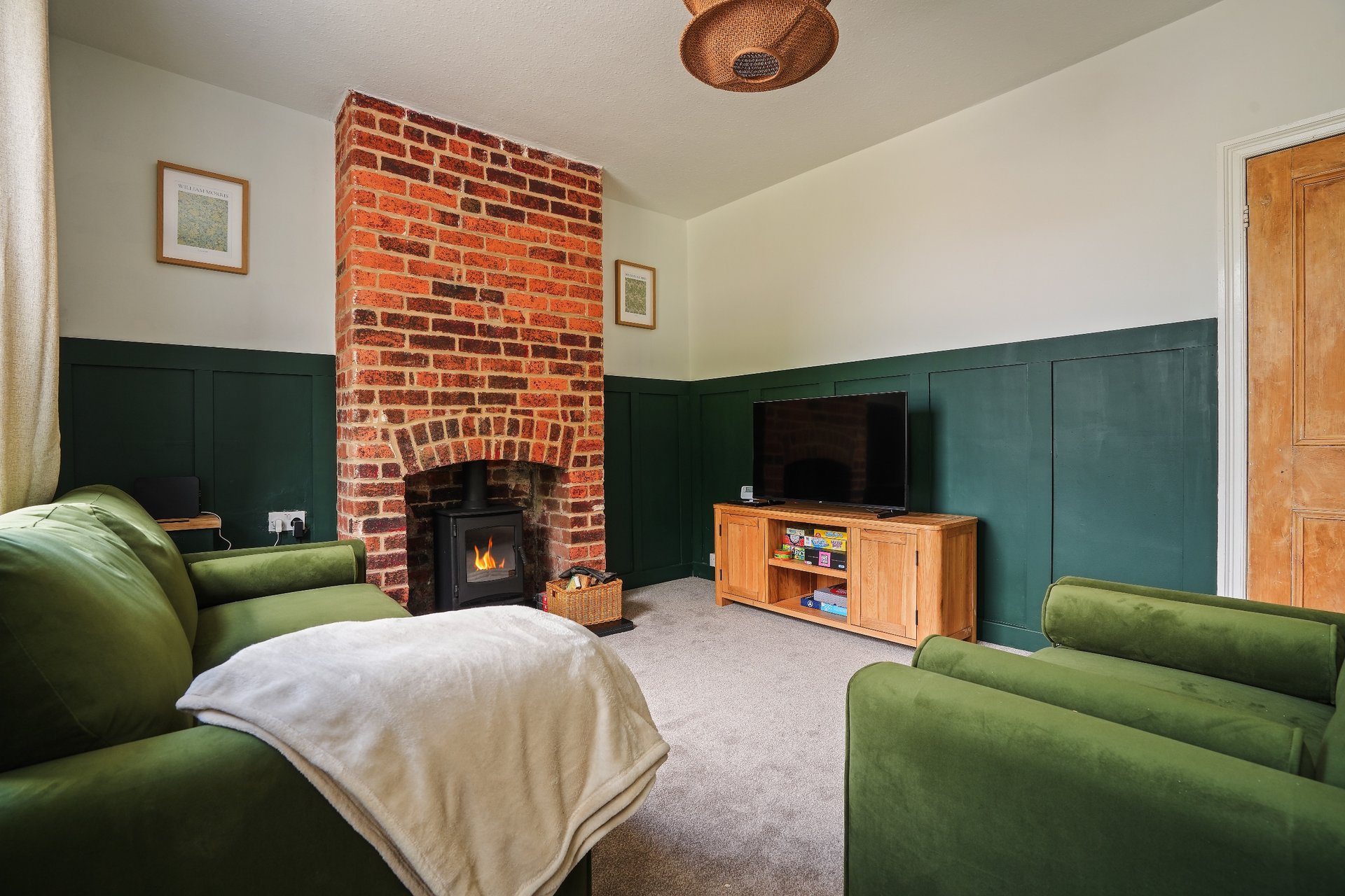 Living room with green seating, brick fireplace, wood TV stand and cream carpet