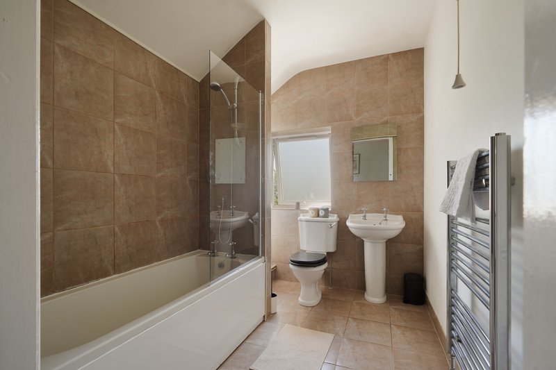 Bathroom with brown tile walls, shower enclosure, pedestal sink and toilet