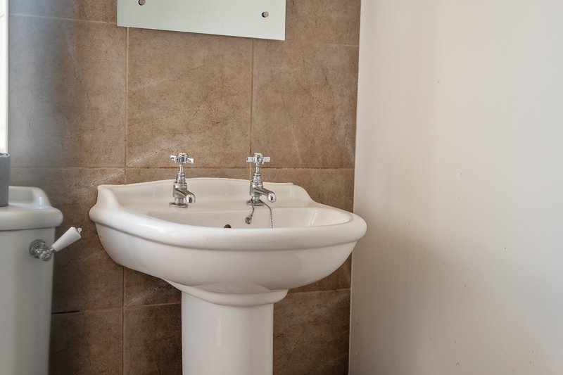 Bathroom with pedestal sink, chrome taps and brown tiled walls