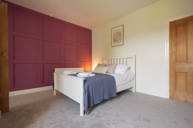 Bedroom with white metal bed frame, burgundy panelled wardrobe, and neutral carpet flooring