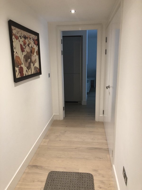 Clean hallway with light wood flooring, white walls, framed artwork, and open doorways