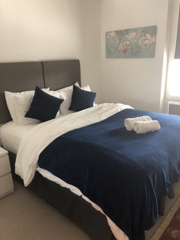 Modern bedroom with dark blue bedding, white pillows, grey headboard and framed artwork