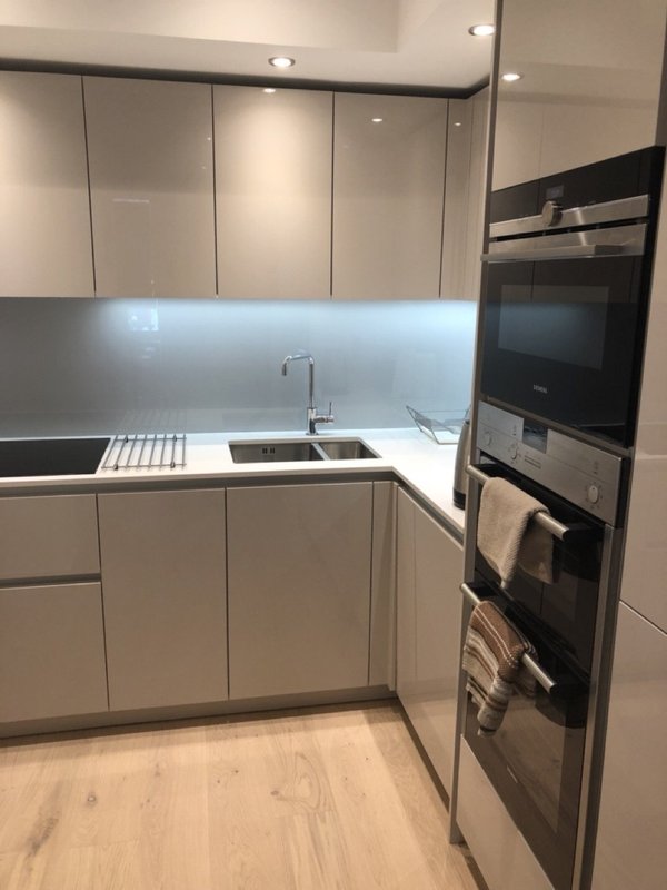 Modern kitchen with white cabinetry, grey backsplash, stainless steel sink and built-in appliances