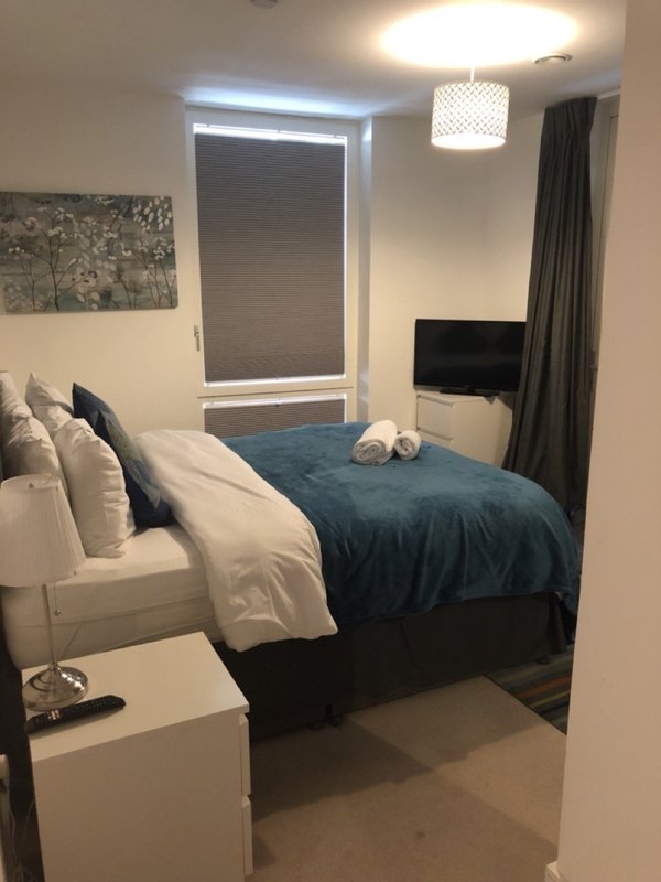 Compact bedroom with double bed, blue bedding, window with blinds, pendant light fixture