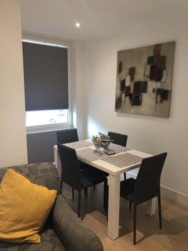 Dining area with white table, black chairs, abstract wall art and yellow cushion