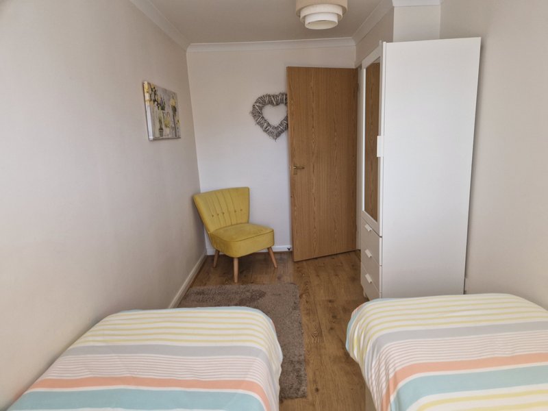 Twin bedroom with striped bedding, yellow chair, wooden door and cream walls