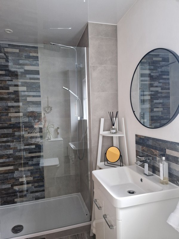 Modern bathroom with walk-in shower, white sink, round mirror and blue tile backsplash