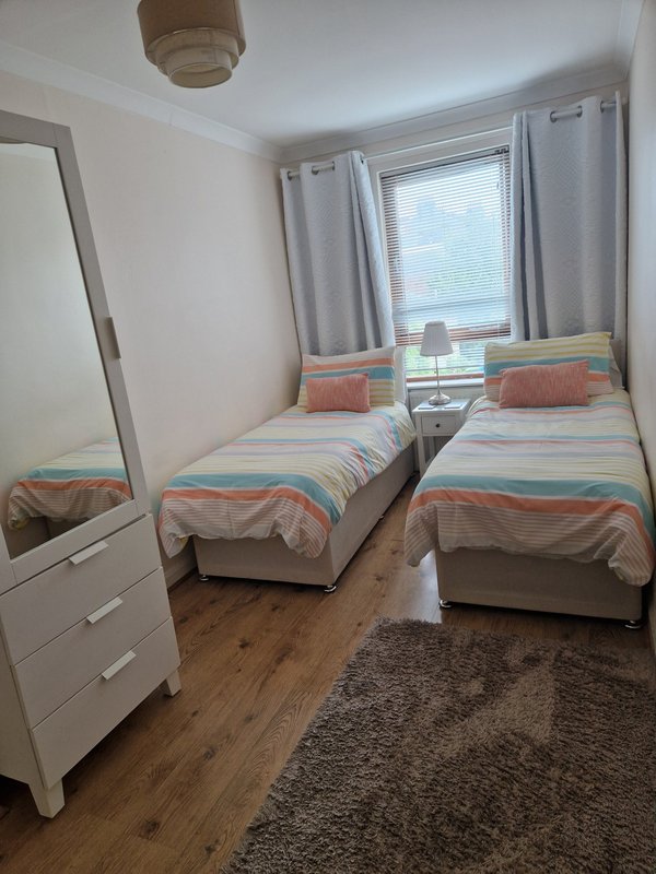 Bedroom with two single beds, striped bedding, wooden floor, white furniture and window with curtains