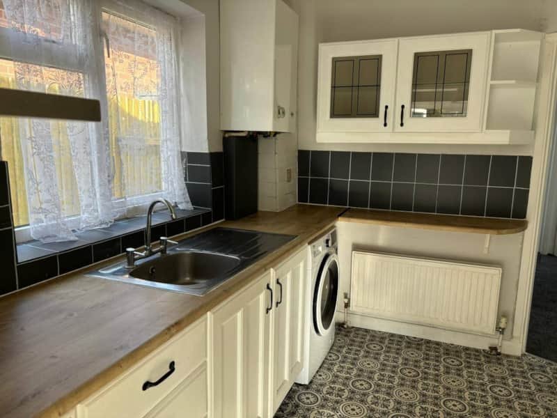 Kitchen with cream cabinets, black tile backsplash, wooden countertop and washing machine