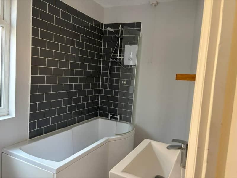 Modern bathroom with black subway tile shower wall, white bathtub and separate sink