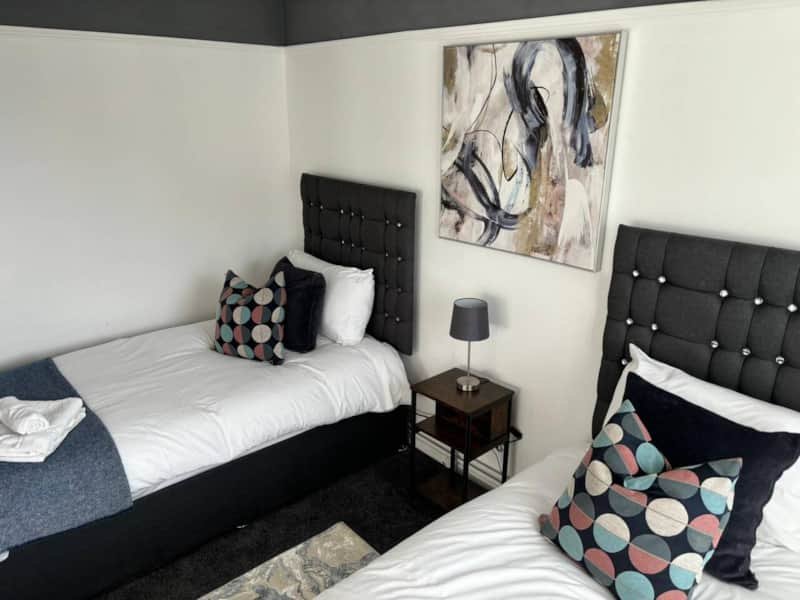 Twin bedroom with black upholstered headboards, white bedding, patterned cushions and wall art