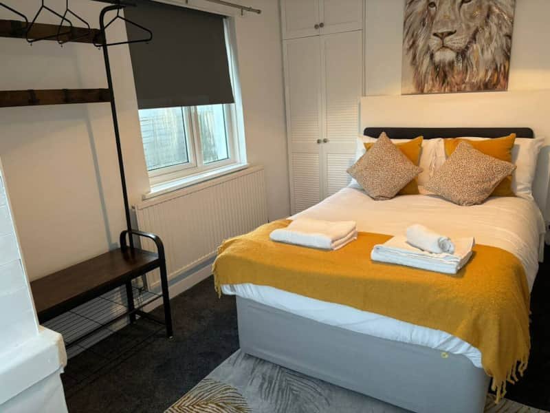 Bedroom with double bed, yellow bedding, lion artwork, window with blind, and coat rack