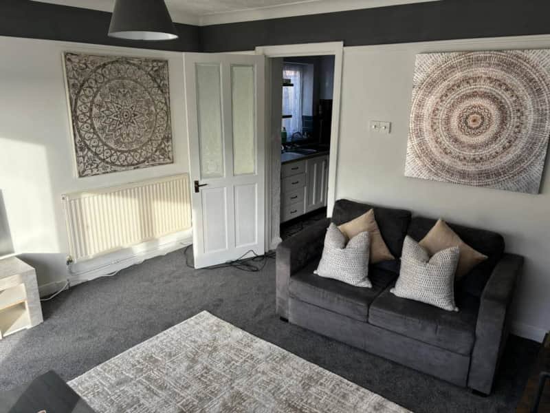 Modern living room with dark sofa, geometric wall art, radiator and open doorway to kitchen