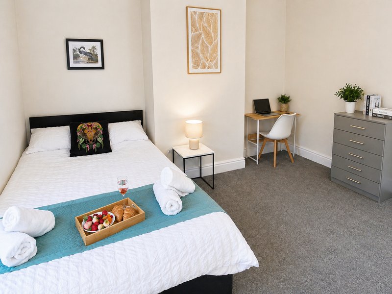 Bedroom with double bed, desk, grey dresser, framed wall art and potted plants