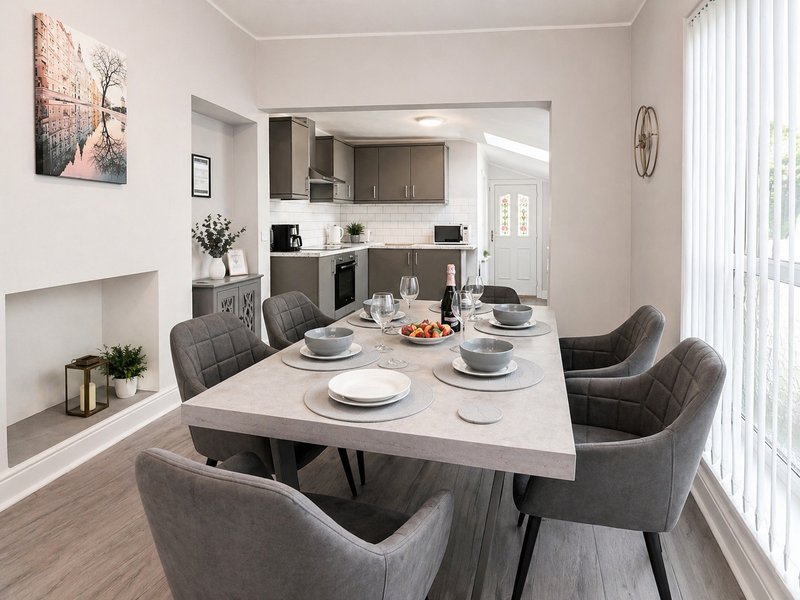 Modern dining room with grey upholstered chairs, light table, and open kitchen visible in background