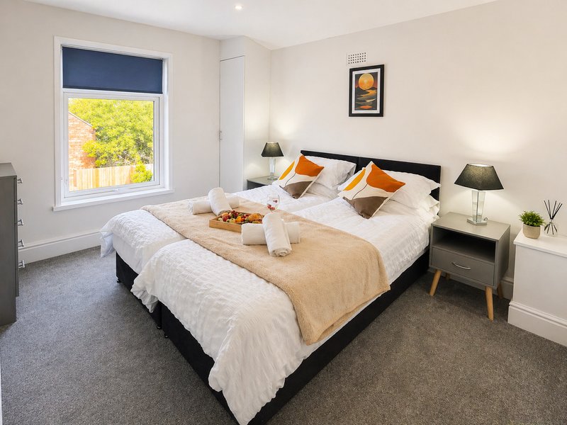 Modern bedroom with double bed, bedside tables, lamps, and window overlooking garden