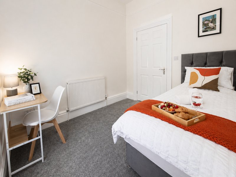 Bright modern bedroom with two beds, desk, radiator, white door and framed wall art