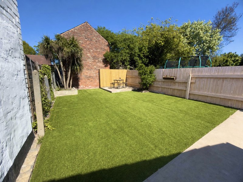 Spacious garden with lawn, brick building, wooden fence and mature trees