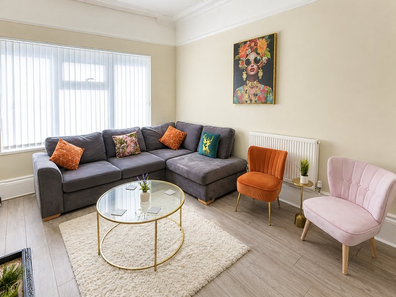 Modern living room with grey corner sofa, pink armchair, round glass table and artwork