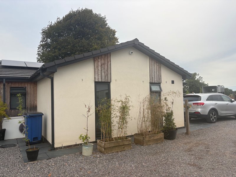 Modern single-story property with cream walls, dark roof, gravel driveway and parked car