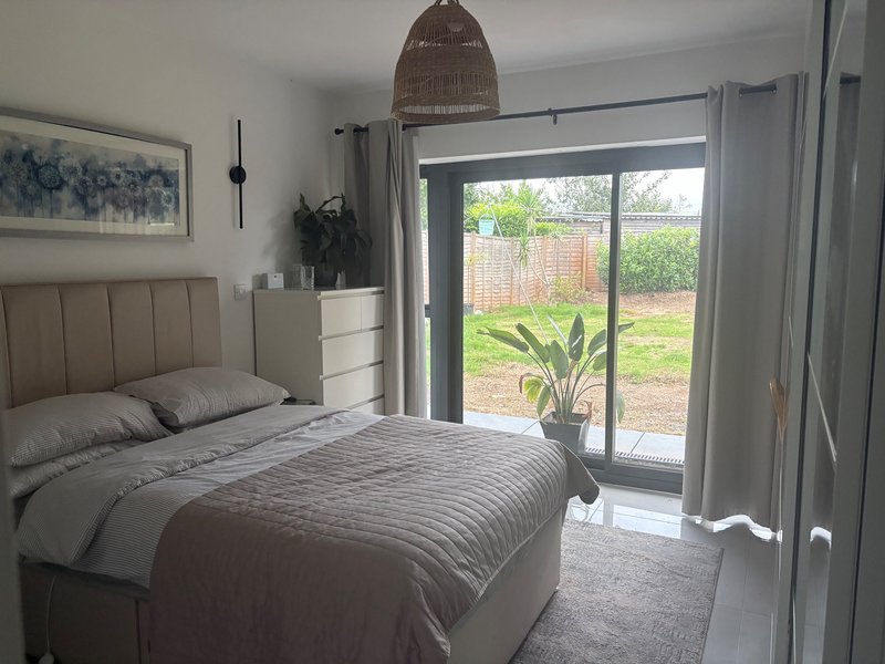 Modern bedroom with double bed, upholstered headboard, pendant lamp, and sliding doors to garden